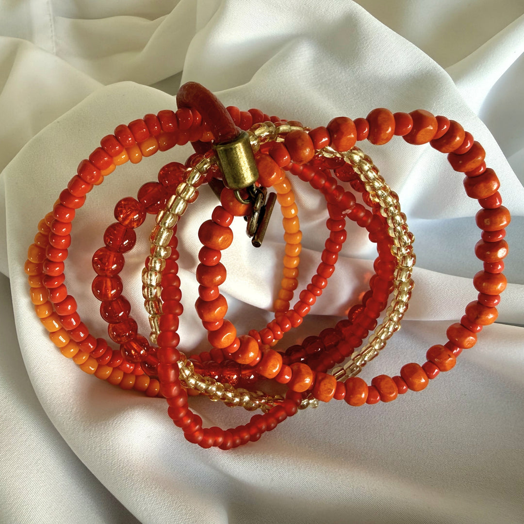 Angled view of a five-strand bracelet showing layered wood and glass beads in warm orange, red, and golden tones.