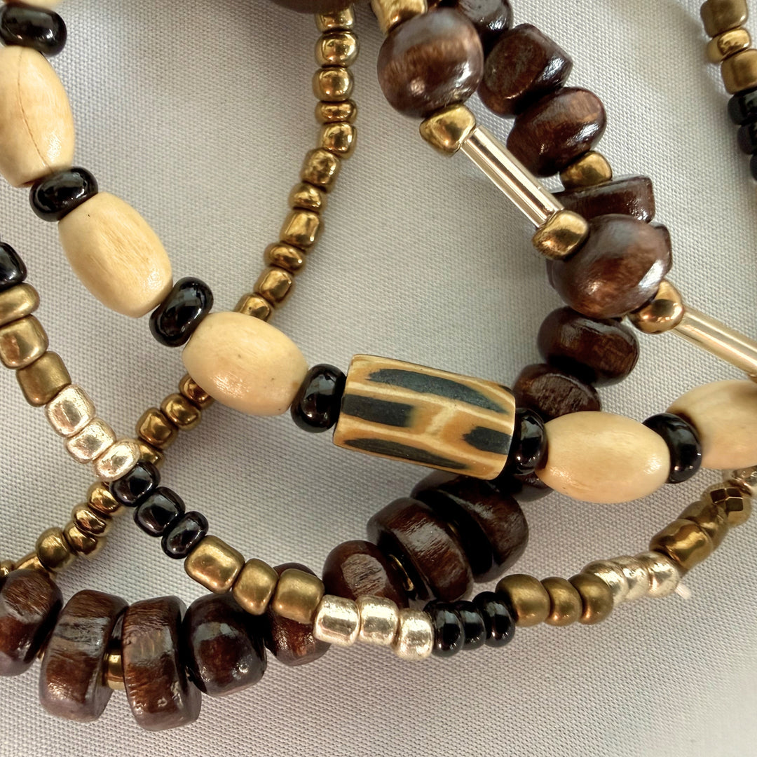 Close-up of a handcrafted multi-strand bracelet showing mixed wood, glass, and polymer clay beads with warm natural tones.