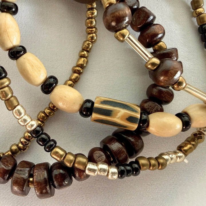 Close-up of a handcrafted multi-strand bracelet showing mixed wood, glass, and polymer clay beads with warm natural tones.