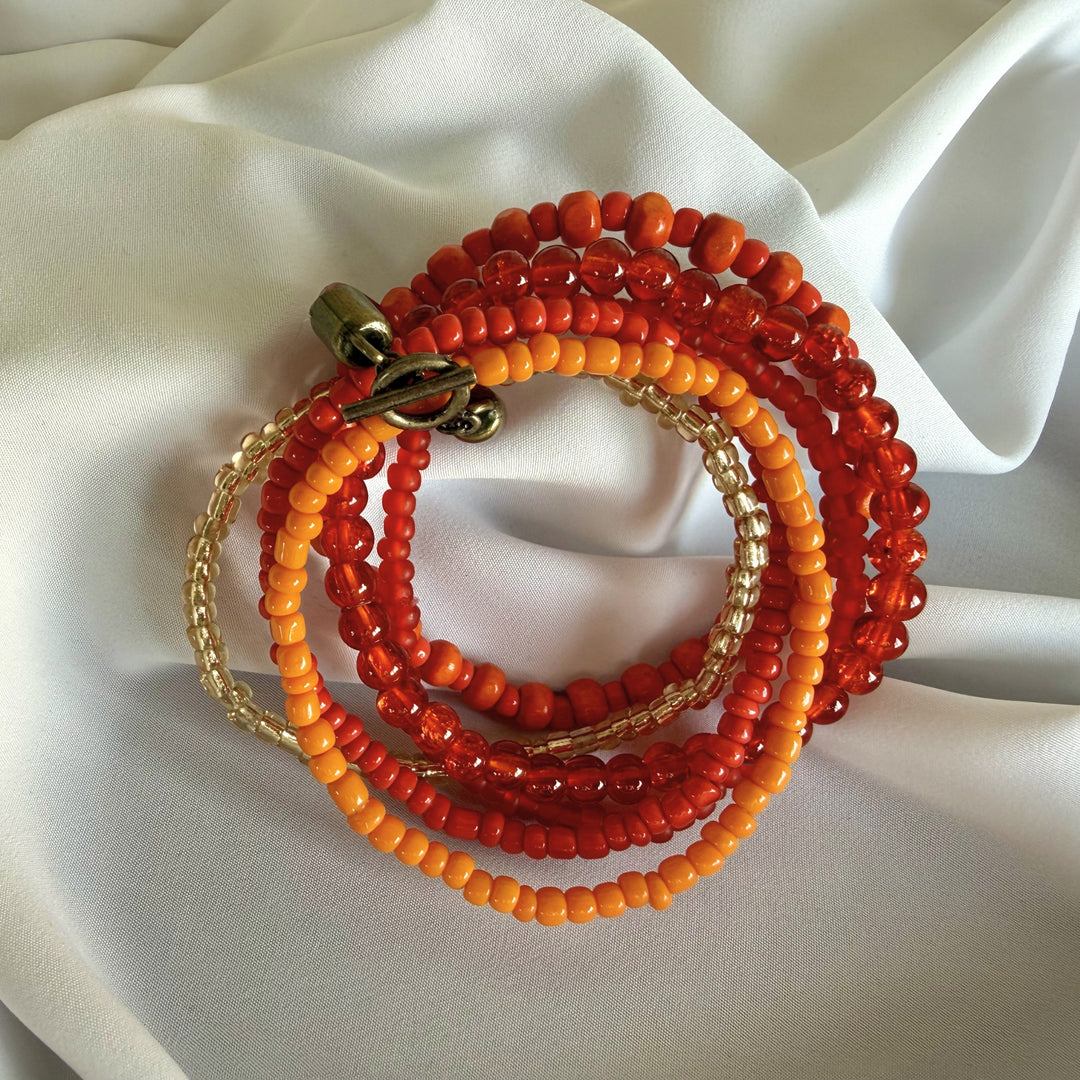 Full view of a handcrafted 5-strand bracelet made with wood and glass beads in orange, red, and golden tones.