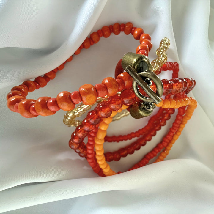 Top view of a handcrafted five-strand bracelet showing layered bead structure in orange, red, and golden tones.