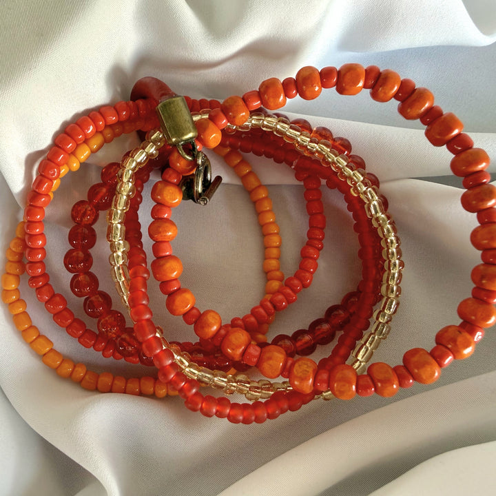 Five-strand beaded bracelet shown spread out, highlighting layered wood and glass beads in warm orange, red, and gold tones.