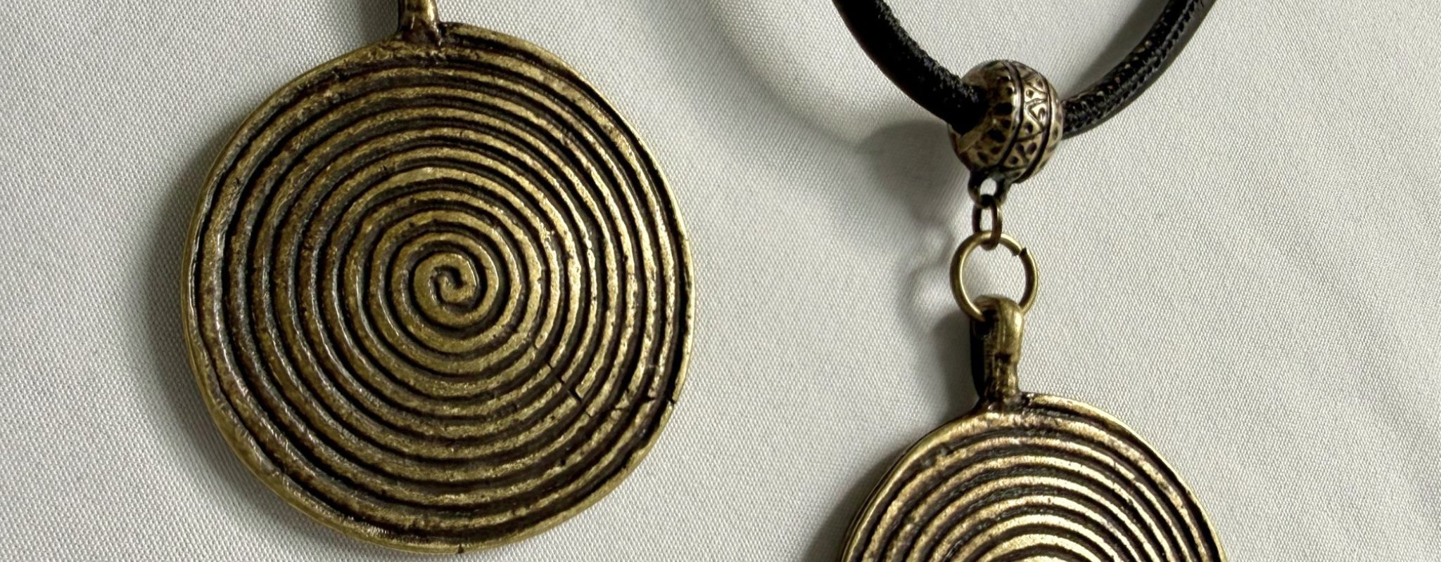 Two spiral pendant necklaces in antique bronze-toned metal and black cork cords.