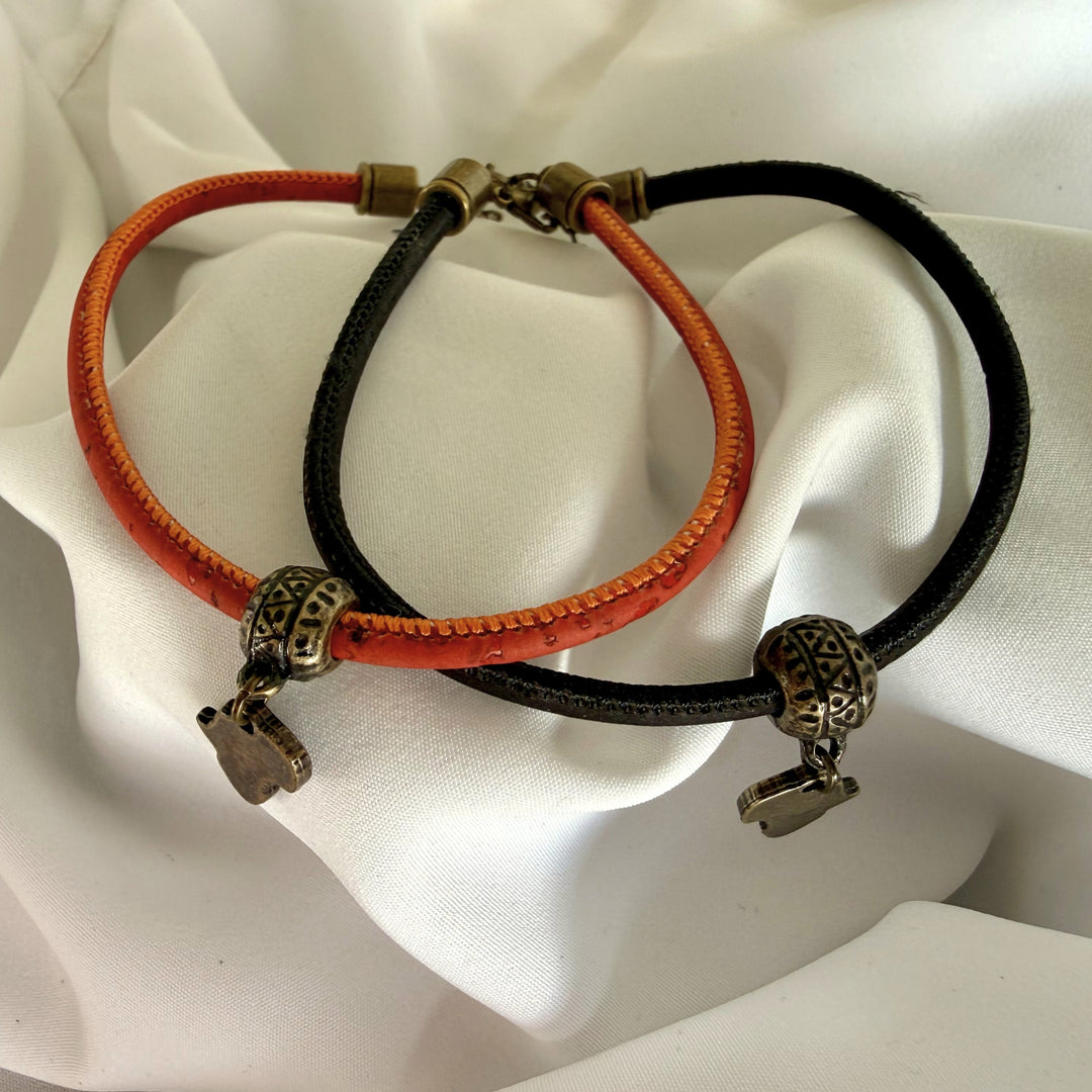 Two separate handcrafted cork bracelets in black and red, each featuring an Africa charm in antique brass finish.