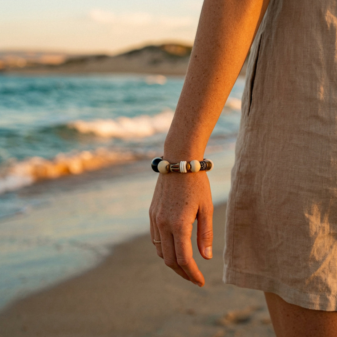 Handcrafted agate and mixed bead bracelet with crackle agate, wood, and polymer clay beads worn on a woman’s wrist while walking along the beach beside the ocean.
