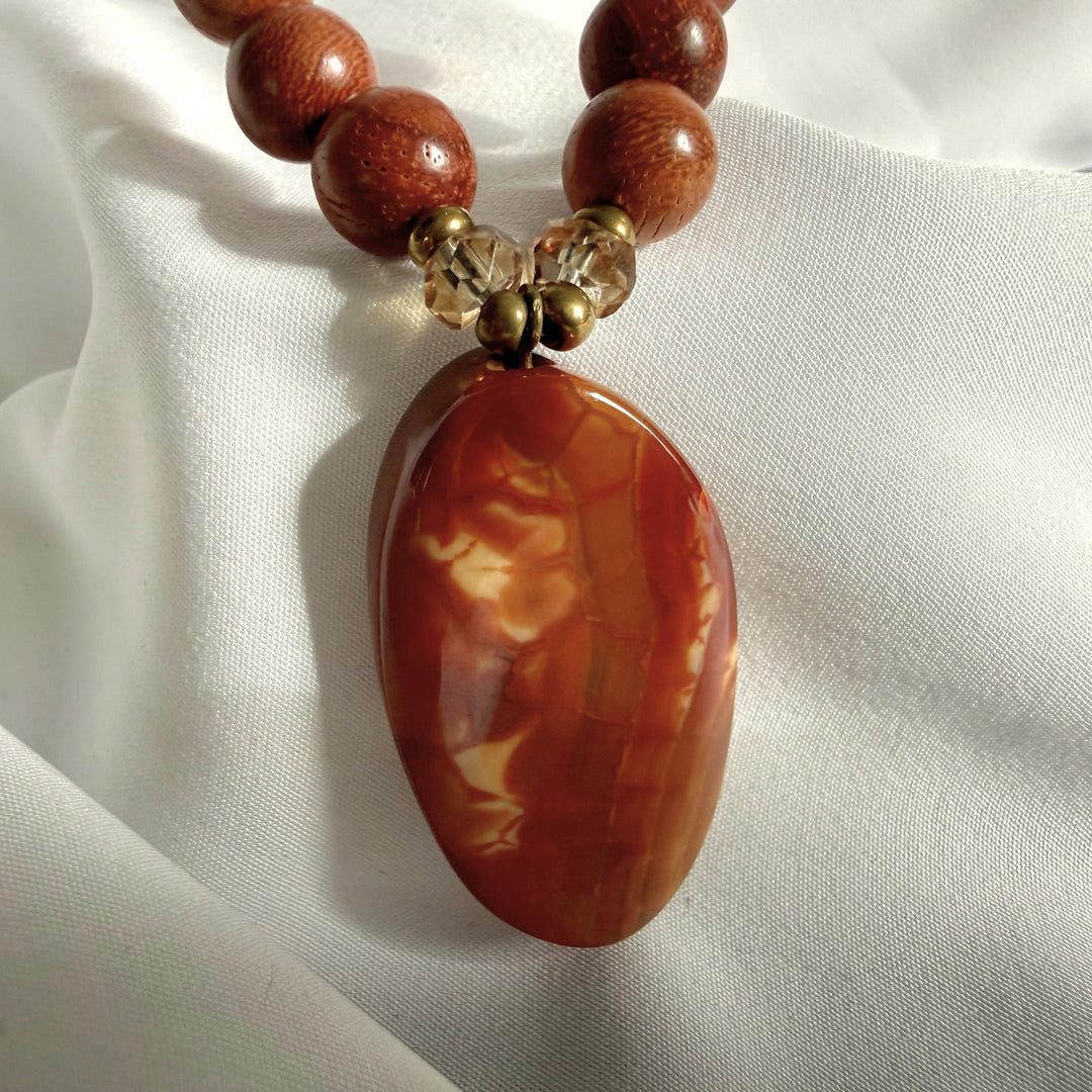 Close-up of oval amber bead pendant on a handcrafted necklace with wooden and mixed accent beads.