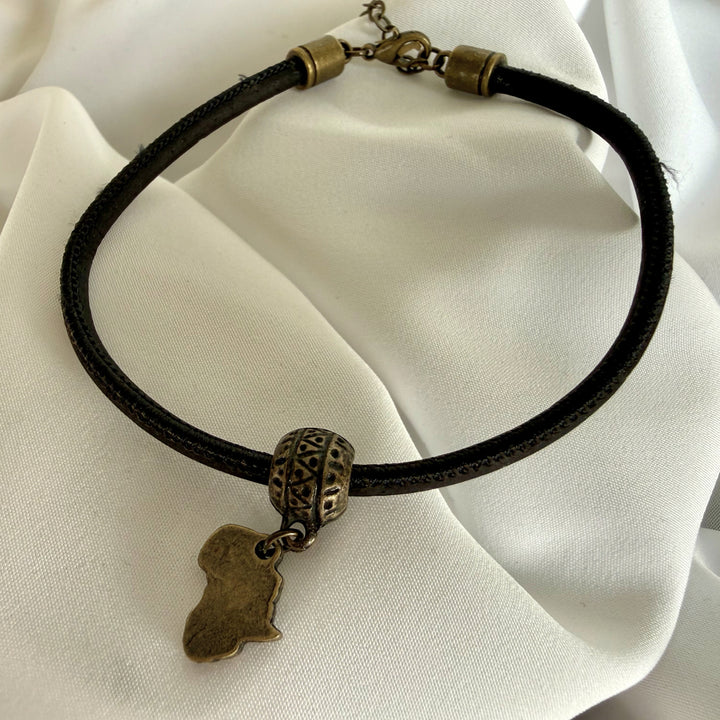 Full view of a handcrafted black cork bracelet with antique brass Africa charm and stainless steel clasp.