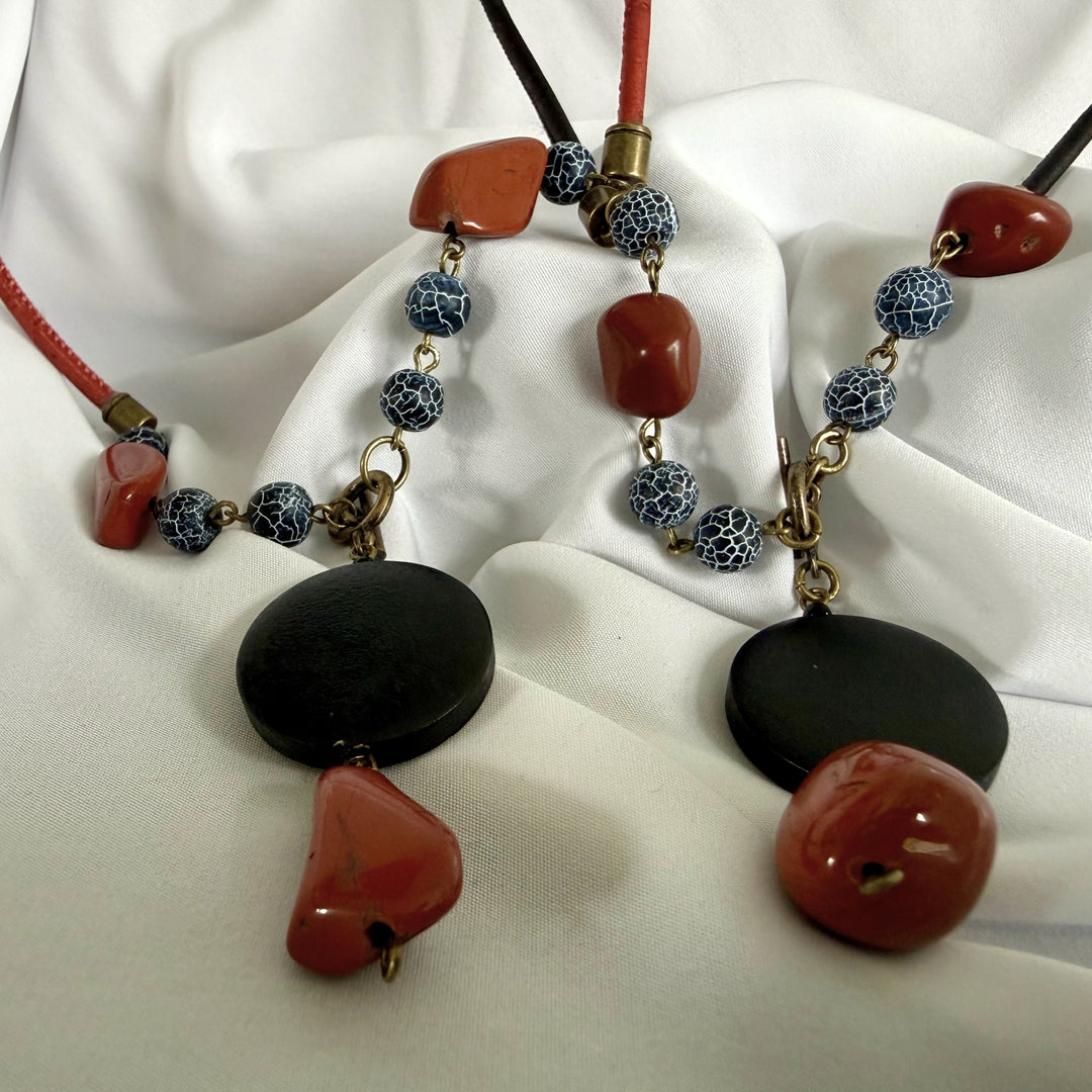 Bottom view of two handcrafted pendant necklaces showing wood, jasper, and agate elements on black and red cord.