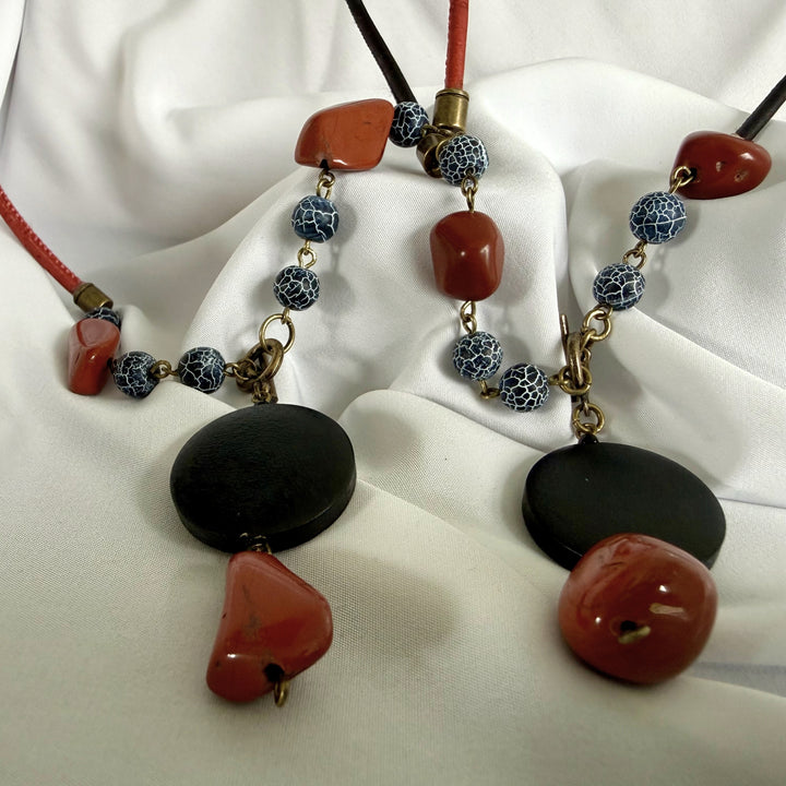 Bottom view of two handcrafted pendant necklaces showing wood, jasper, and agate elements on black and red cord.