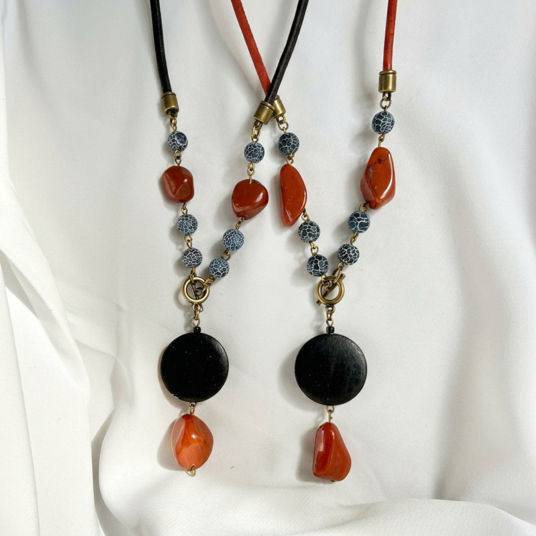 Top view of two handcrafted pendant necklaces shown in black and red cork cord with wood and natural stone details.