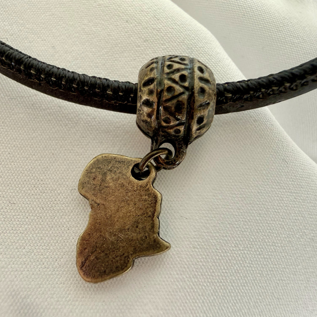 Close-up of Africa charm on a black cork bracelet with antique brass finish and metal accents.