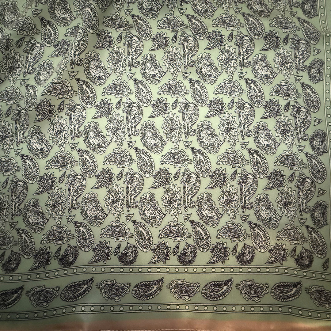 Close-up of black and white paisley pattern on soft green silk fabric.