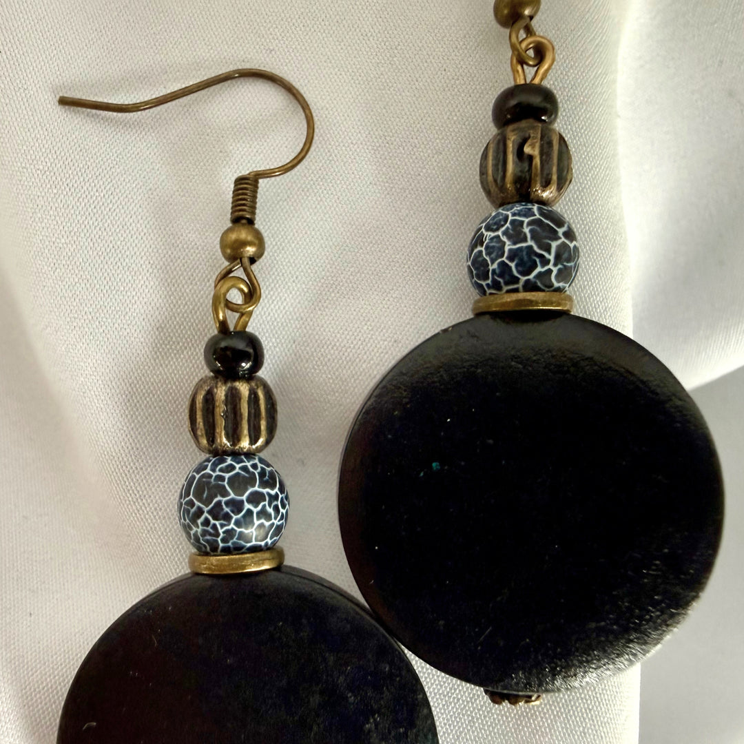 Close-up of a pair of handcrafted earrings made with black wooden beads and black crackle agate stones.