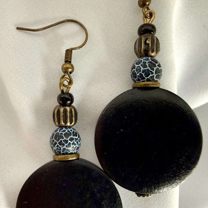 Close-up of a pair of handcrafted earrings made with black wooden beads and black crackle agate stones.