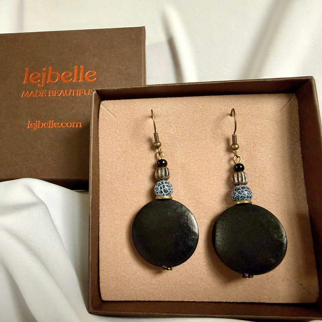 Handcrafted drop earrings with black wood and crackle agate beads displayed in a brown jewellery box with logo branding.
