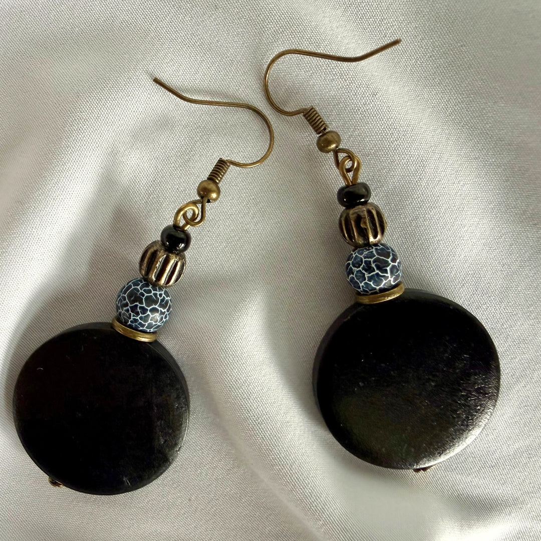 Two handcrafted drop earrings laid apart showing black wood beads and crackle agate bead details.