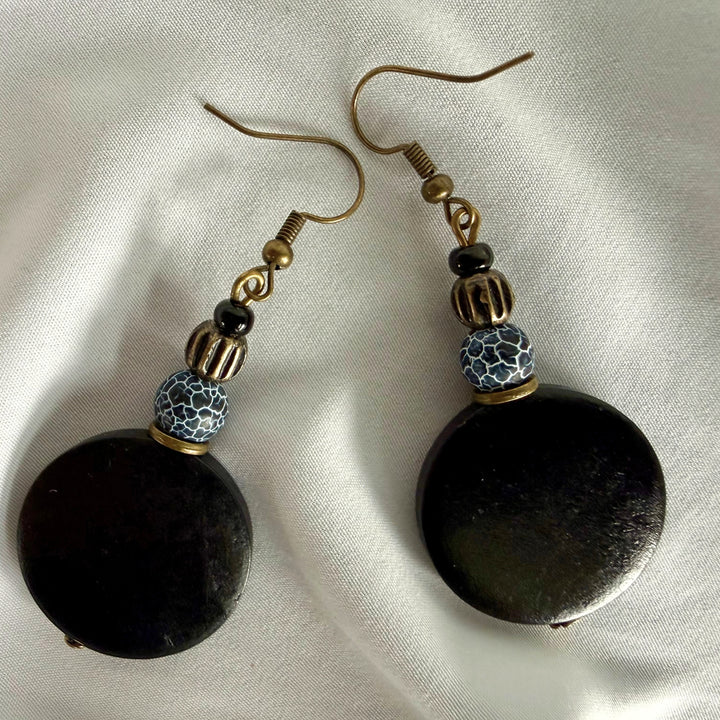 Two handcrafted drop earrings laid apart showing black wood beads and crackle agate bead details.