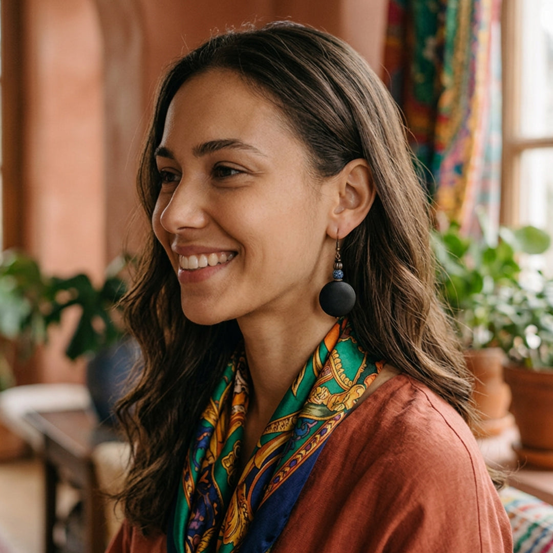 Black wood and crackle agate drop earrings worn by a relaxed woman in an earthy-toned indoor environment.