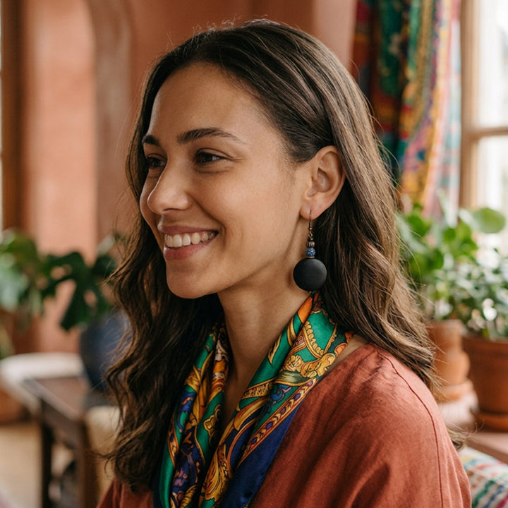 Black wood and crackle agate drop earrings worn by a relaxed woman in an earthy-toned indoor environment.