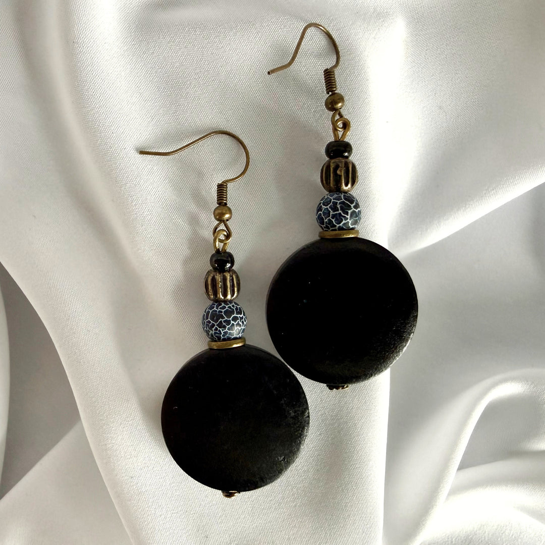 Top view of handcrafted drop earrings featuring black wood beads and crackle agate beads on silk fabric.