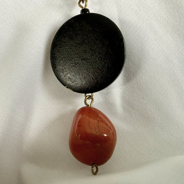 Close-up of black wooden pendant combined with red jasper stone in a handcrafted necklace design.