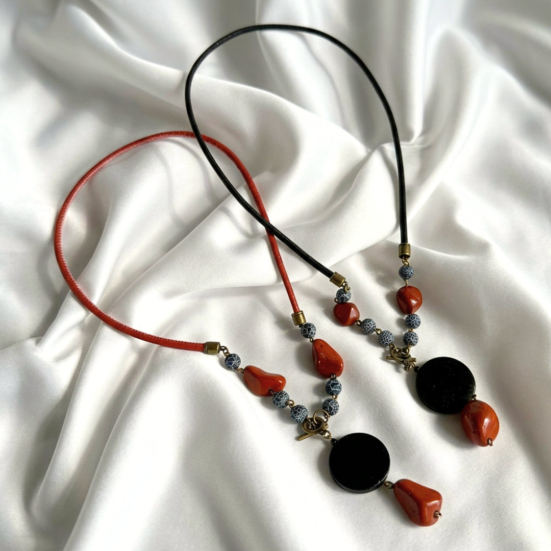 Full view of two handcrafted pendant necklaces in black and red cork cord featuring black wood, red jasper, and crackle agate.