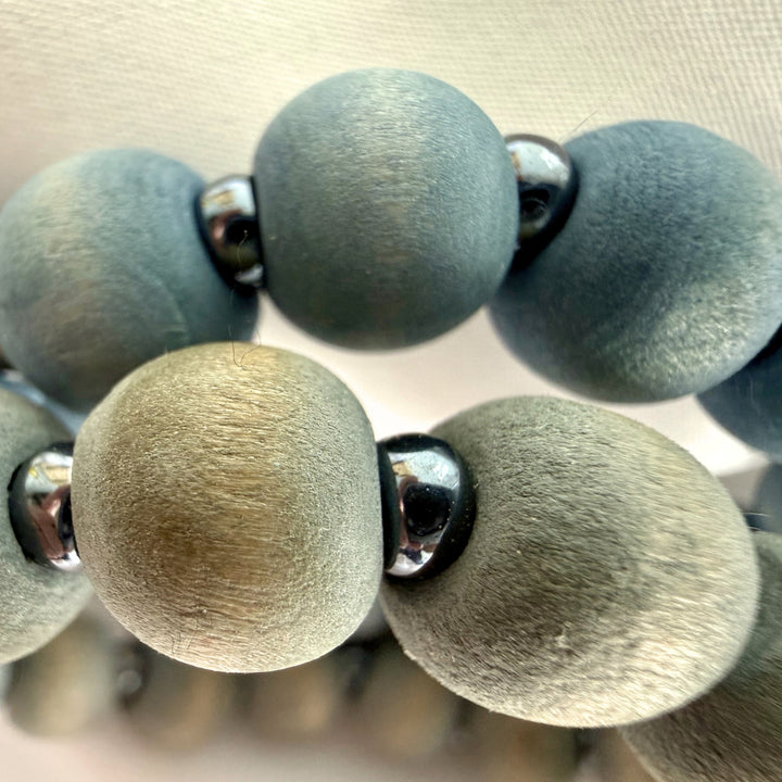 Extreme close-up of layered blue and grey wood bead bracelets with silver-coloured seed bead accents.