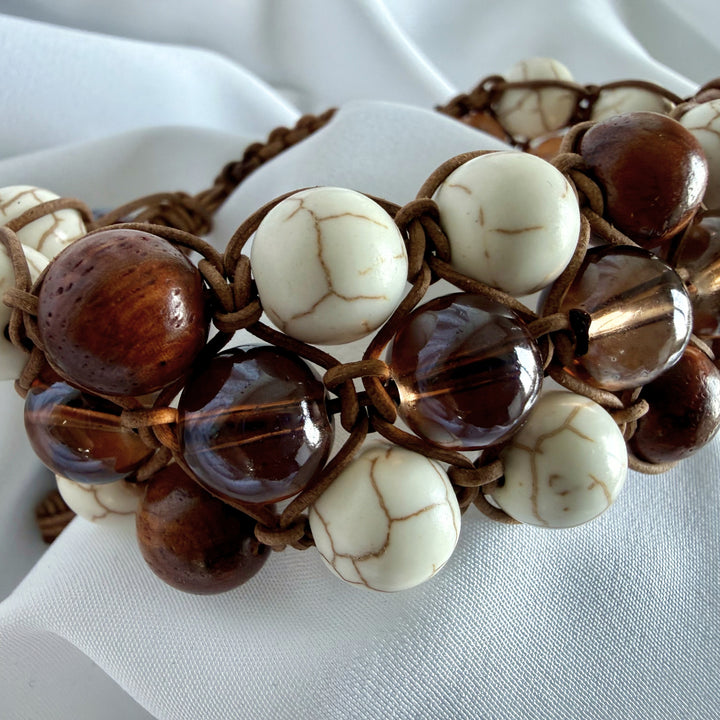 Angled view of a handmade macramé bracelet featuring white howlite stones, wood beads, and glass beads.