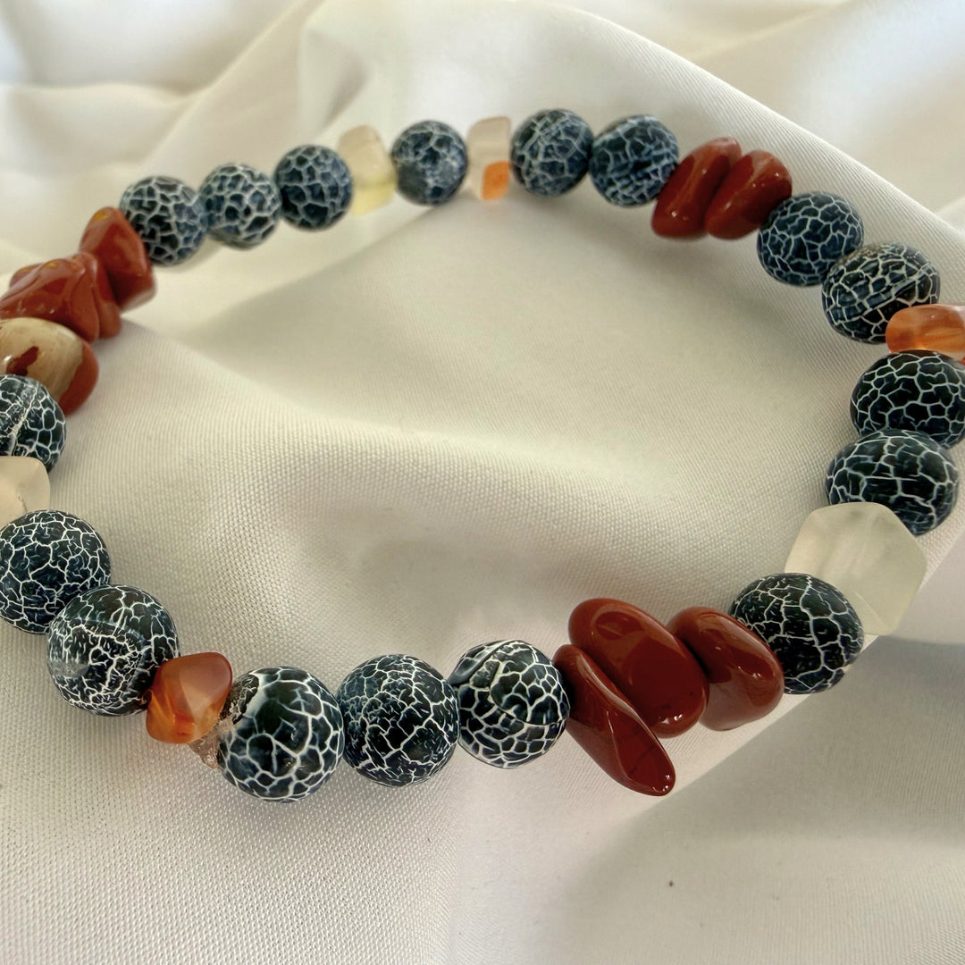 Angled view of a handcrafted beaded bracelet featuring warm carnelian tones and dark black crackle agate stones.