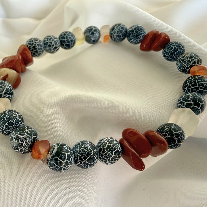 Angled view of a handcrafted beaded bracelet featuring warm carnelian tones and dark black crackle agate stones.