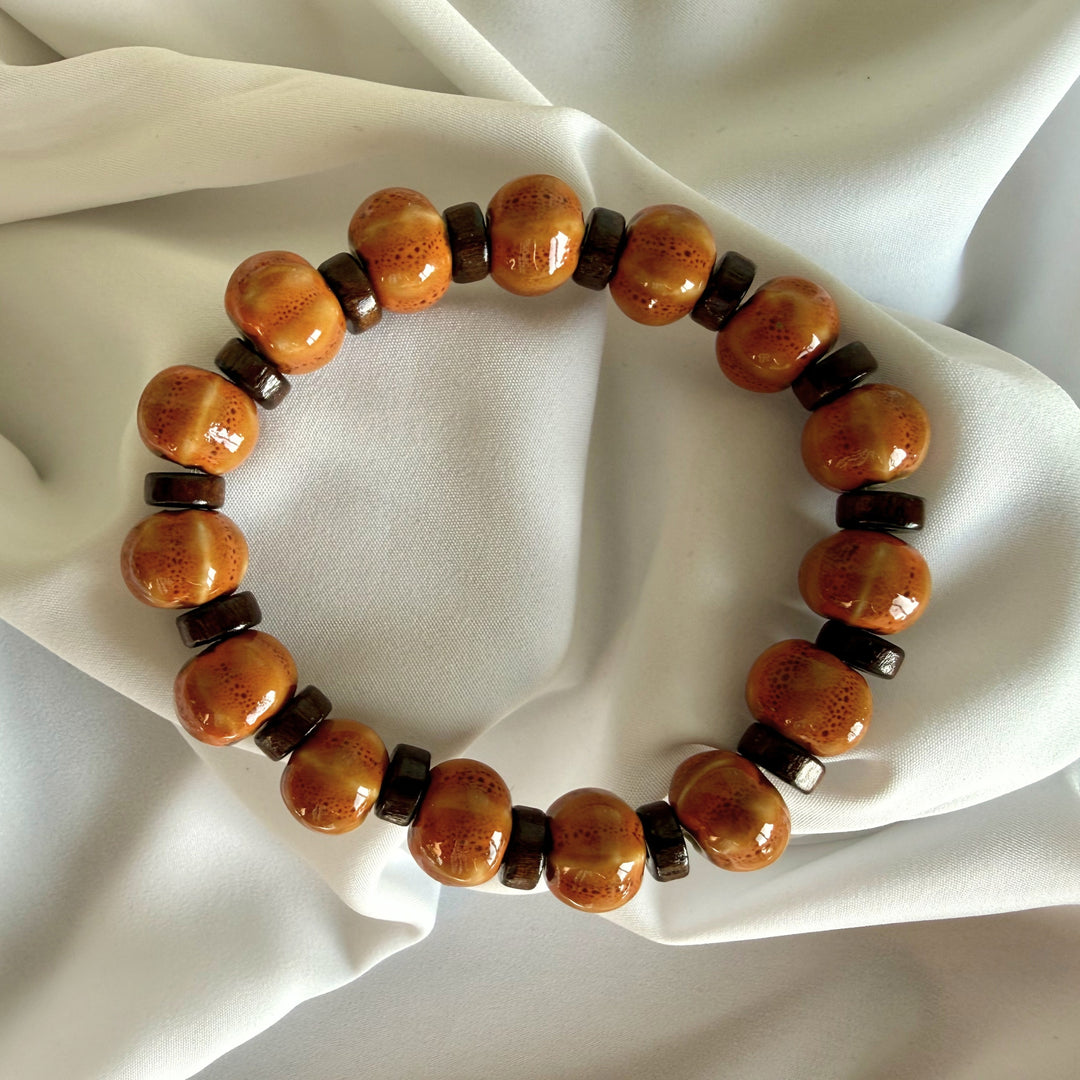 Full view of a handcrafted bracelet made with light brown ceramic beads and flat wood beads in warm earthy tones.