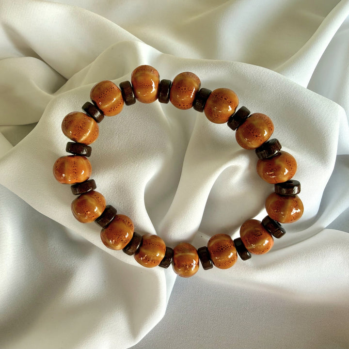 Full view of a handcrafted ceramic and flat wood beaded bracelet showing warm light and dark brown tones on elastic cord.