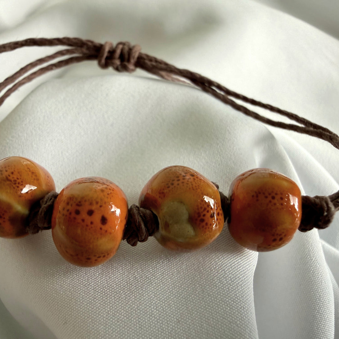 Front view of a ceramic bead bracelet with light brown beads and natural hemp cord.