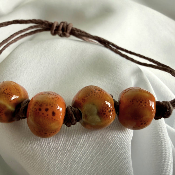 Front view of a ceramic bead bracelet with light brown beads and natural hemp cord.