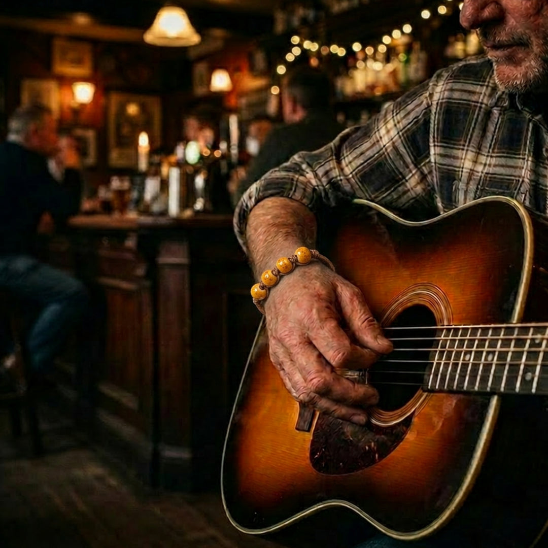 Handcrafted ceramic beaded bracelet with dark brown hemp cord worn by a man playing guitar in a pub.
