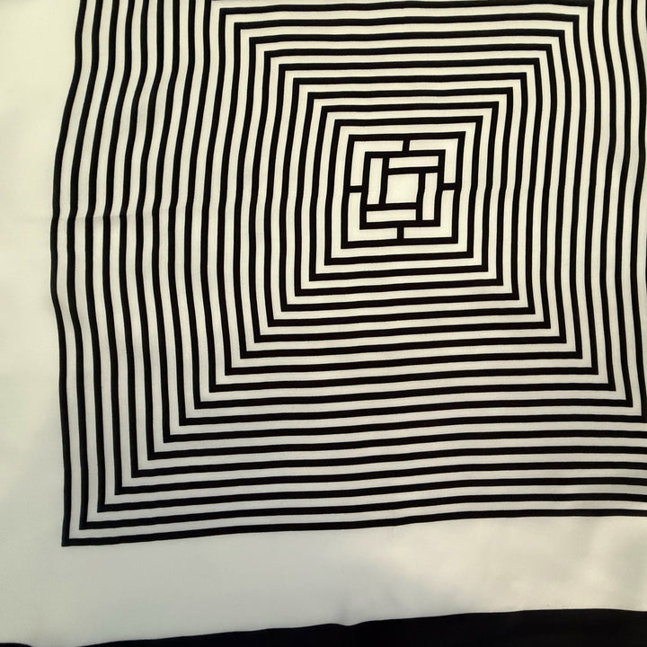 Close-up view of the intricate black and ivory labyrinth geometric pattern printed on smooth mulberry silk fabric.