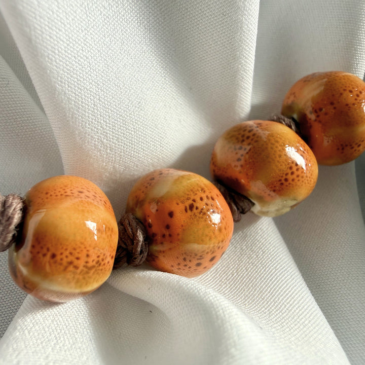 Close-up of smooth ceramic beads and textured dark brown hemp cord on a handmade bracelet.