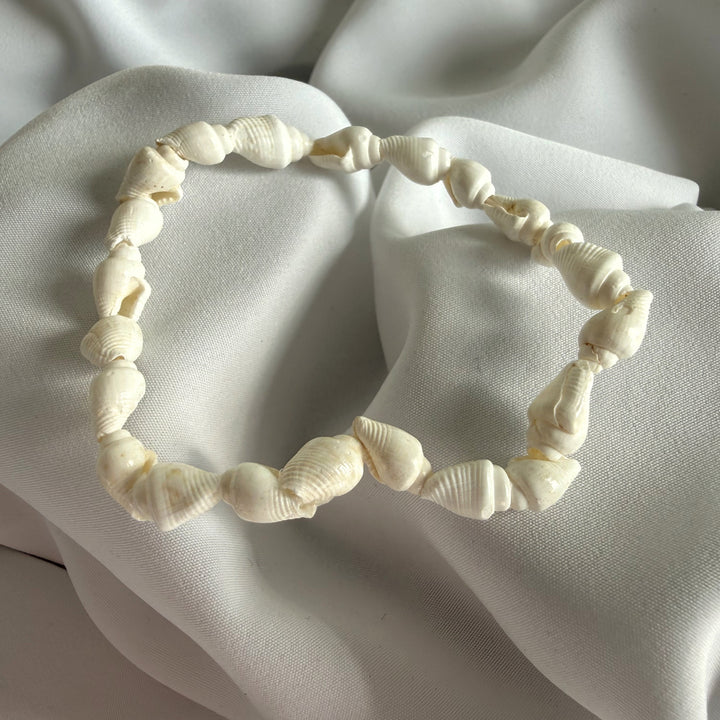 Full view of a handcrafted bracelet made with natural white cowrie shells on elastic cord.