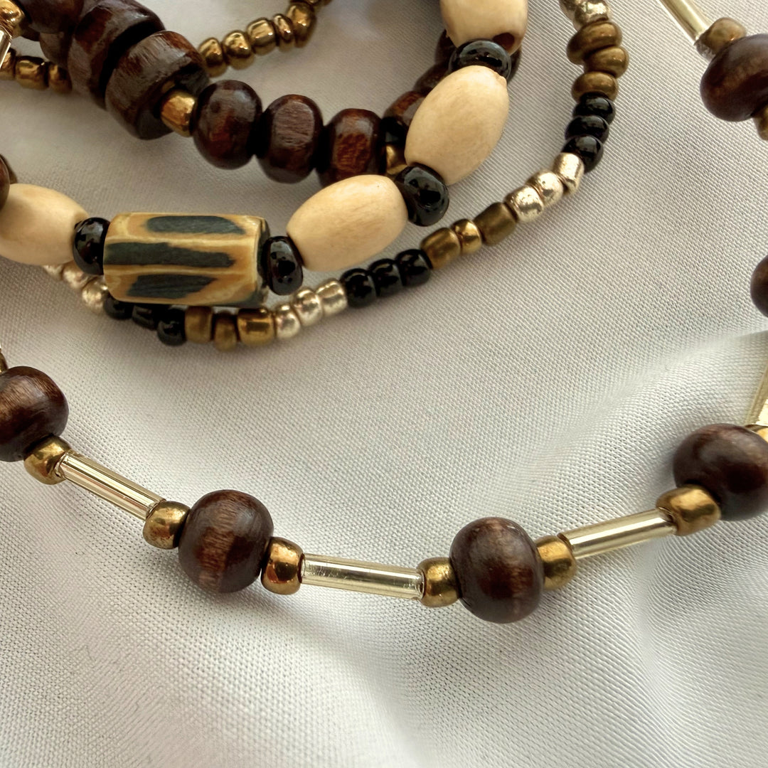 Close-up of dark brown wood beads paired with gold-toned accents on a layered beaded bracelet.