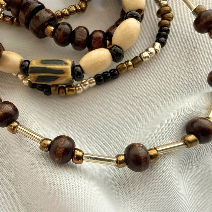 Close-up of dark brown wood beads paired with gold-toned accents on a layered beaded bracelet.