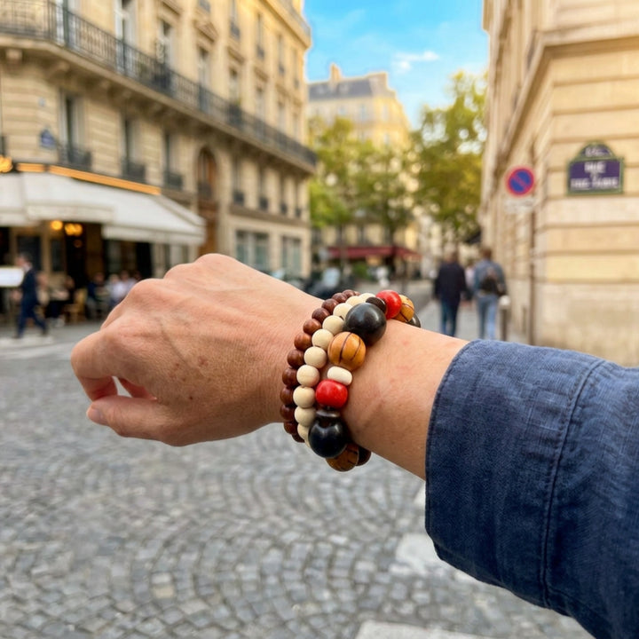 Set of three handcrafted beaded bracelets with wood and howlite beads worn on a woman’s wrist while walking through sunny streets in Paris.