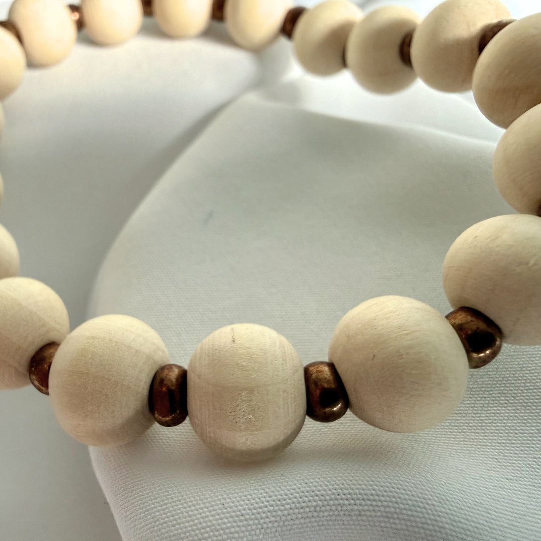 Close-up of a handcrafted bracelet showing ivory wood beads with golden seed bead accents.