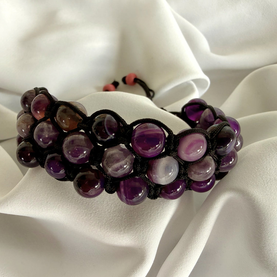 Handcrafted amethyst macramé bracelet with natural purple stones resting on white silk fabric.