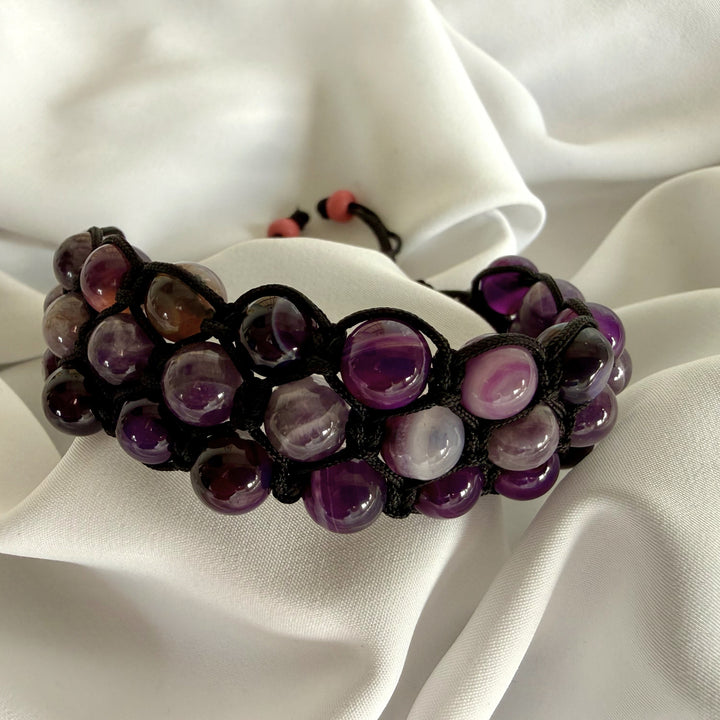 Handcrafted amethyst macramé bracelet with natural purple stones resting on white silk fabric.