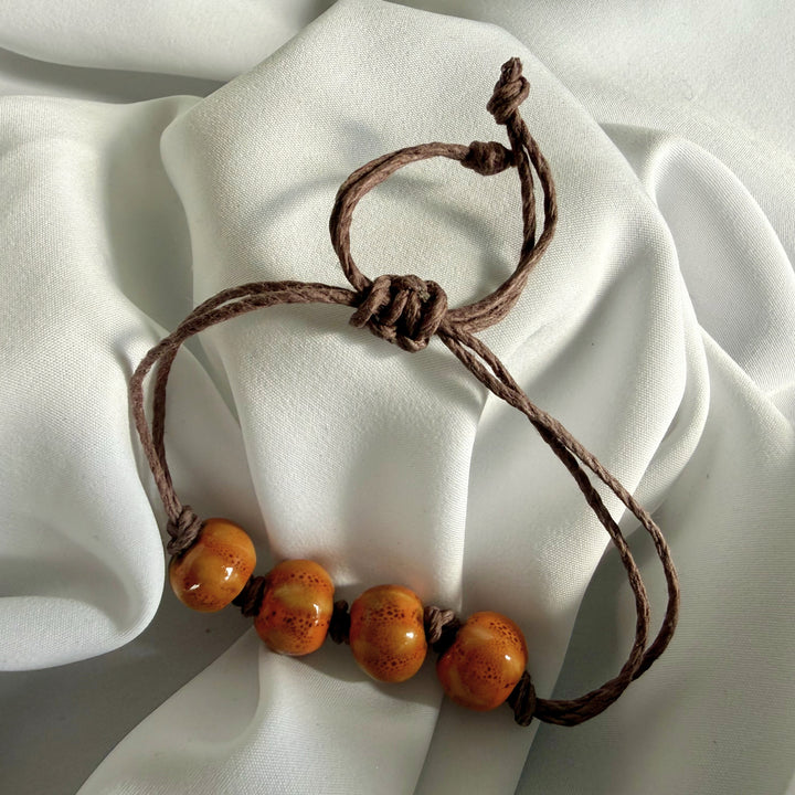 Full view of a handcrafted ceramic beaded bracelet with dark brown hemp cord.