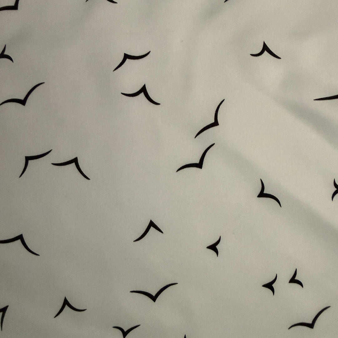 Close-up of black V-shaped bird motifs on ivory silk fabric.