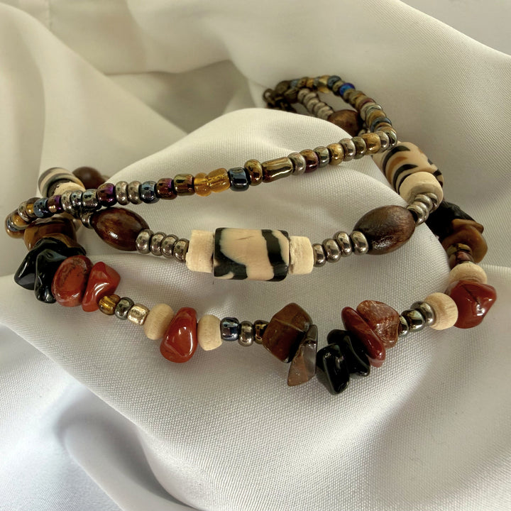 Angled view of a layered bracelet featuring African print beads, seed beads, wood, and semi-precious chip stones in earthy tones.