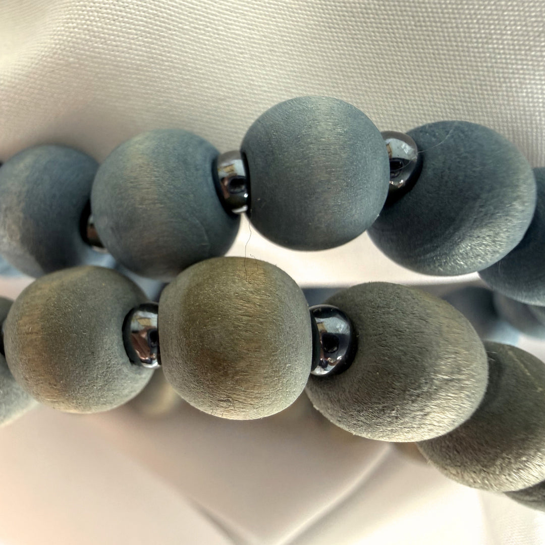 Close-up of two beaded bracelets placed on top of each other showing layered blue and grey wood beads with silver seed bead details.