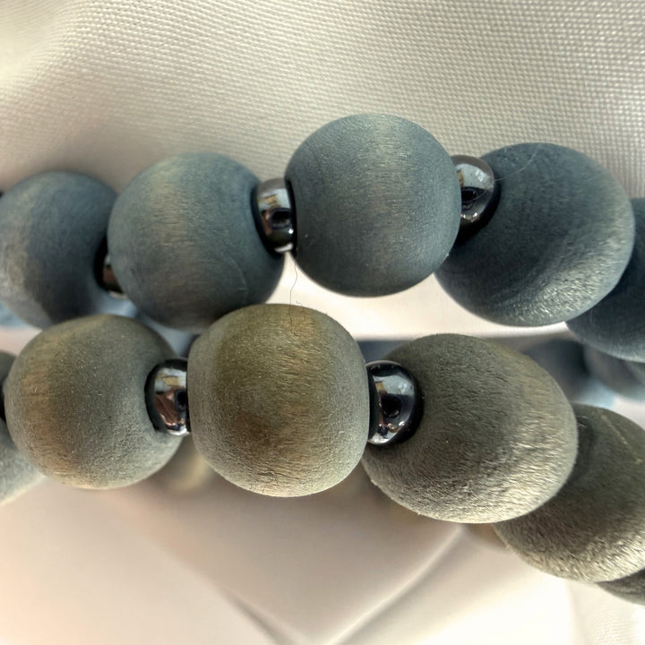 Close-up of two beaded bracelets placed on top of each other showing layered blue and grey wood beads with silver seed bead details.