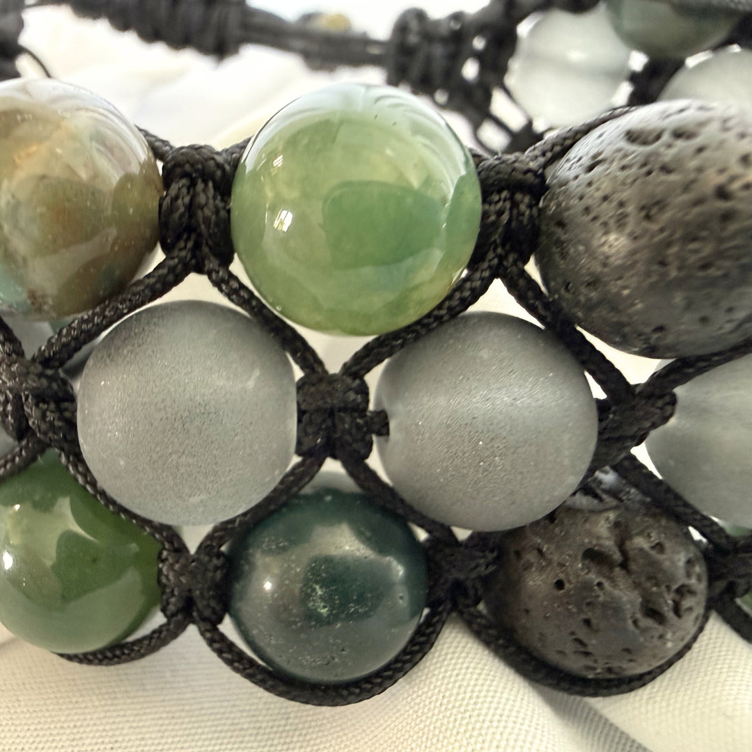 Close-up of green moss agate beads with black beads and detailed macramé knotting on a handcrafted bracelet.